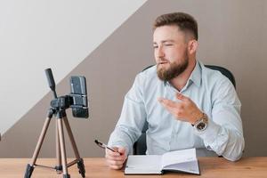 Smiling bearded business man, filming his video blog episode using smartphone photo