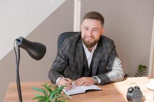 Businessman writing notes while sitting at his desk. Young bearded man photo