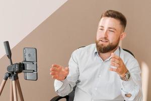 Smiling bearded business man, filming his video blog episode using smartphone photo