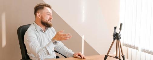 Cheerful bearded young man leading an online meeting using smartphone writing photo