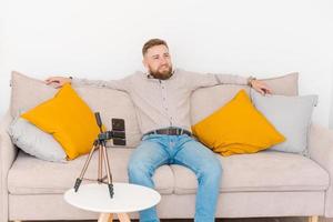 Smiling bearded guy filming video using smartphone on tripod online while photo