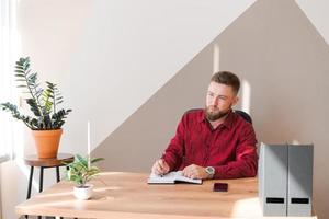 Budget planning. Pensive bearded man writing in a notebook while sitting photo