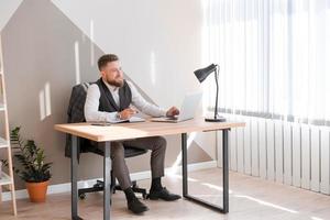 Caucasian bearded business man is sitting at window table using his laptop photo