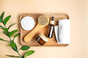Amber glass cosmetics bottles on wooden tray with ruskus leaves and white towels. Set of natural organic SPA beauty products on beige background top view. Body and face skin care concept photo