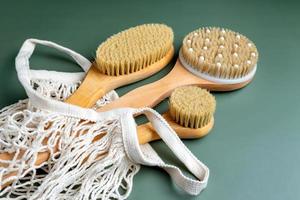 primer plano de un baño cepillos de bambú para masaje seco en bolsa de algodón mwsh sobre fondo verde. spa en casa y herramientas de relajación foto