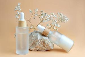 close up of collagen cream in glass jar, serum in frosted glass bottle and dry flowers on beige background. Set for skin and body care beauty products. photo