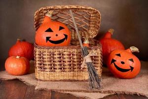 Halloween pumpkins in a wicker box with a broom on a dark background photo