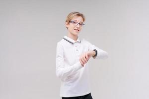 un niño feliz con gafas y una camisa mira su reloj o rastreador de fitness. foto