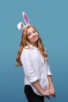 Girl in pink rabbit ears on her head on blue studio background. Cheerful photo