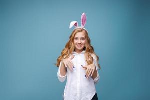 Girl in pink rabbit ears on her head on blue studio background. Cheerful photo