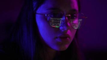 Young woman in a dark purple room uses a laptop video