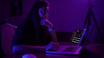 Young woman in a dark purple room uses a laptop