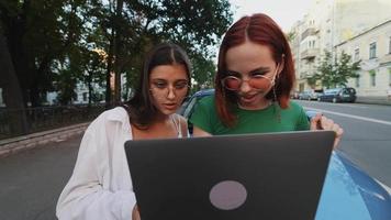 två ung kvinnor se på en bärbar dator närliggande en avstannade bil video
