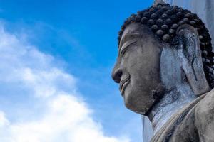 detail of the face of a representation of the buddha with his eyes closed, on blue nature sky background, the from under view photo