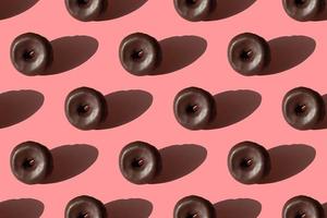 patrón de alimentos sin fisuras de sabrosos donuts glaseados de chocolate con sombras sobre un fondo rosa foto