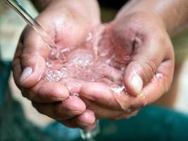 agua clara que fluye de una fuente de agua potable en las palmas de los hombres ahuecados. humedad que da vida en un día caluroso. foto