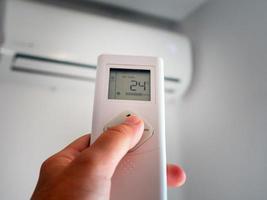 Hand with remote control and adjusting temperature of air conditioner on a white wall. Unfocused background. photo