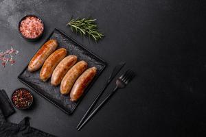 Tasty grilled sausages with spices and herbs on a black slate plate photo