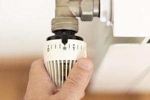 Hand turning off thermostat on heating radiator. Gas price Energy crisis concept photo