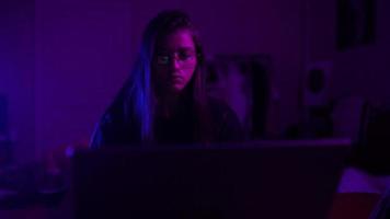 Young woman in a dark purple room uses a laptop video