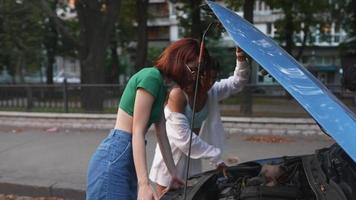 Zwei junge Frauen schauen unter die Motorhaube eines Autos video