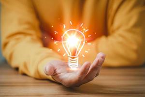 Man holding a glowing abstract light bulb on a wooden table, business problem solving ideas and creative marketing ideas Inventing and learning new things. photo