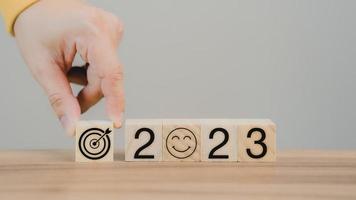 Hand putting wooden cube block with goal icon and 2023 icon on table background. Start new year 2023 with goal plan for work, action plan, strategy, new year business vision. photo