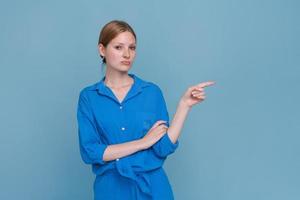 Portrait lovely youth wearing blue shirt pointing with index finger in copy photo