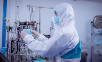 Technician worker wearing protective suite , glove are inspect ion with check  face mask manufacturing process to safe and against from virus. photo