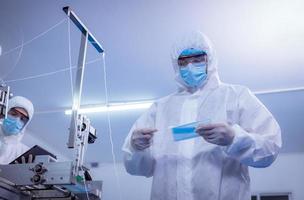 trabajador técnico que usa una suite protectora, los guantes se inspeccionan con el proceso de fabricación de máscaras faciales para asegurarse y evitar el virus. foto