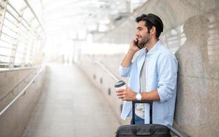 The man using the smartphone while the other hand holding a cup of coffee and pulling the luggage at the airport. photo