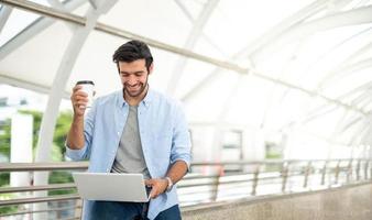 Young caucasian man holding cup of coffee and working on freelance project using portable computer at outer office. photo