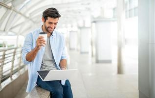 Young caucasian man holding cup of coffee and working on freelance project using portable computer at outer office. photo
