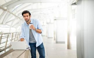 Young caucasian man holding cup of coffee and working on freelance project using portable computer at outer office. photo