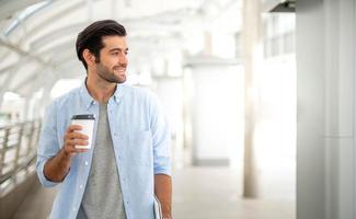 Young caucasian man holding cup of coffee and working on freelance project using portable computer at outer office. photo