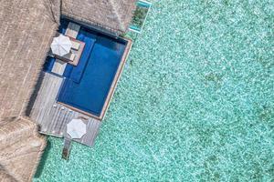 Aerial beach resort. Minimalist beach view from drone or airplane, infinity swimming pool near blue sea lagoon with beautiful ripples and waves. Luxury water villa, umbrella, chairs. Beautiful travel photo