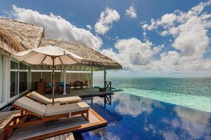 hermoso complejo de villas de agua de lujo, piscina infinita, sillas de playa. cielo soleado y tranquilo, fondo de la playa de la laguna oceánica. pareja vacaciones de verano viajes de vacaciones. isla paradisíaca, paisaje de viaje foto