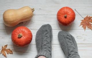 Legs of a girl in knitted socks on a wooden background next to pumpkins and autumn leaves photo