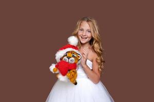 el niño juega con un lindo juguete de tigre de navidad con un vestido blanco en marrón foto