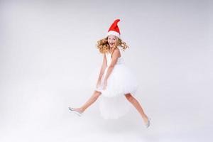 Joyful pretty girl in Red Santa Claus Hat and white dress Laughs and jumps photo