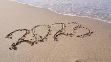 Hand-drawn numbers 2023 of new year on wet yellow sand on beach, copy space. video