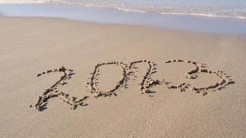 Hand-drawn numbers 2023 of new year on wet yellow sand on beach, copy space. video