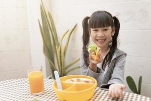 Happy young asian girl eating breakfast and orange juice on the table at home. healthy eating, food and snacks, Ham and Cheese Sandwich photo