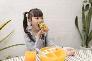 Happy young asian girl eating breakfast and orange juice on the table at home. healthy eating, food and snacks, Ham and Cheese Sandwich photo