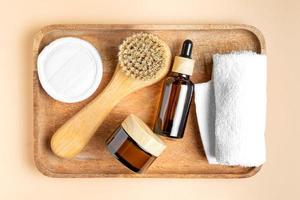 top view of wooden tray with face care products. Beauty oil and daily cream in dark glass backaging. Face brush and cotton towel. Spa treatment. Organic cosmetics photo