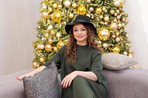 One woman alone at home, sitting on sofa in green cozy suit and black hat photo