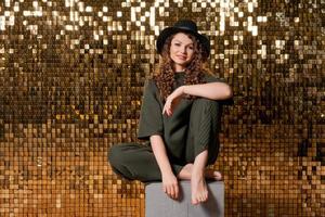 Happy beautiful girl in black hat in studio against background shiny golden