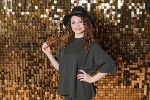 Happy beautiful girl in black hat in studio against background shiny golden photo