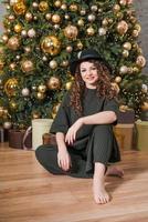 Young beautiful woman sits on floor near Christmas tree and presents New Year's photo