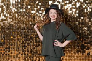 Festive mood in beautiful young woman on background shiny golden wall, smiles photo